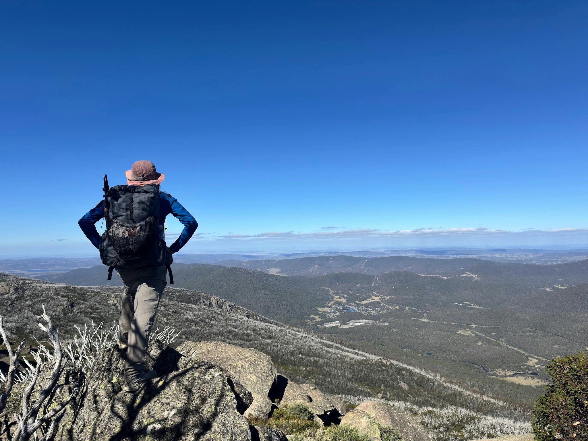 A hiker standing atop some rocks looking down at a town below
