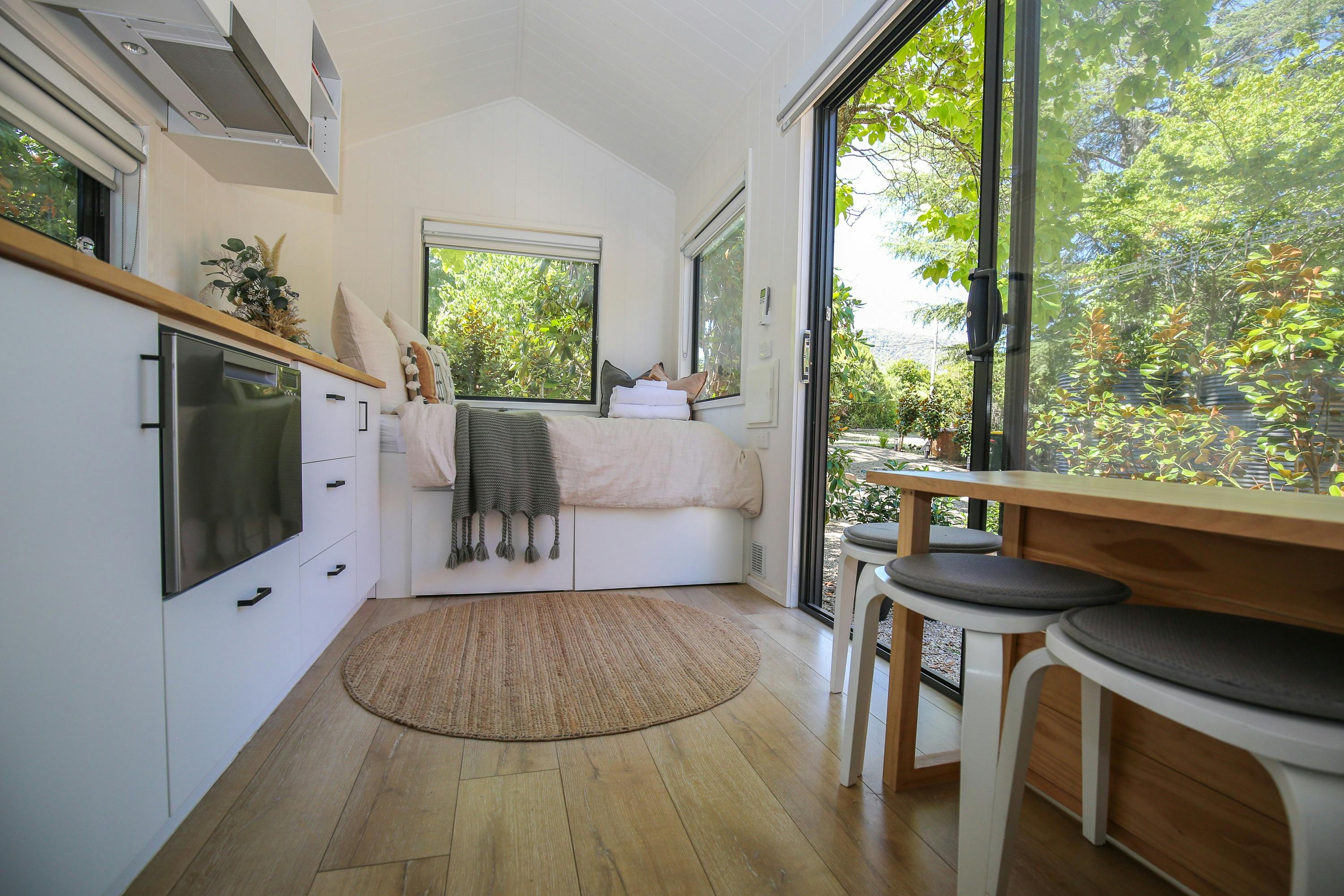 bed, kitchen counter top, small table and stools at the maple tiny home