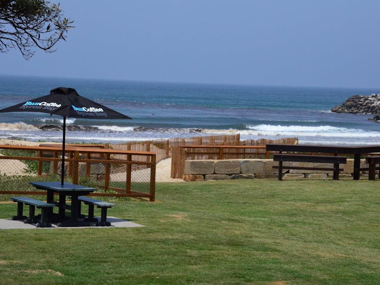 Image shows picnic tables with main beach in the background.