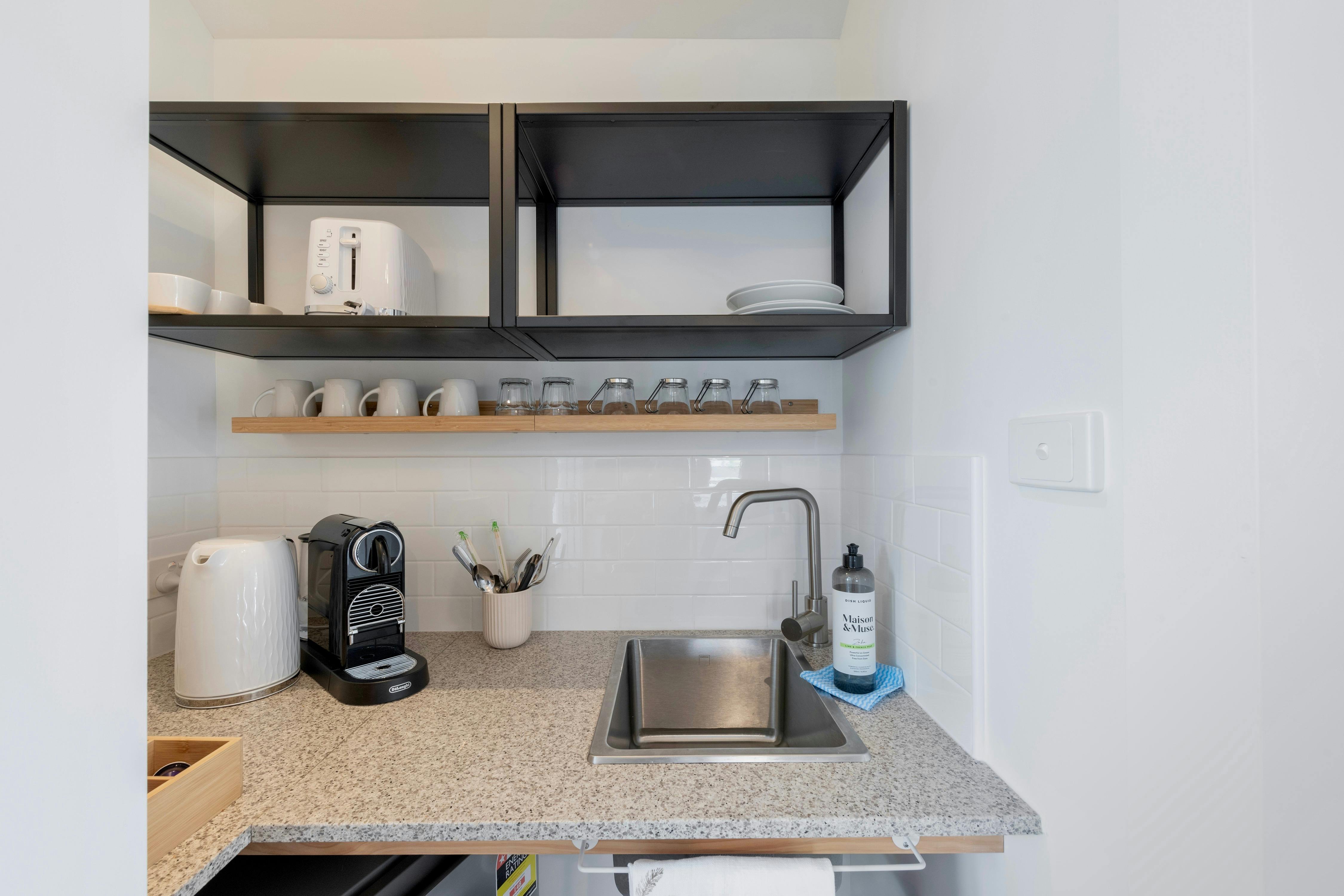 シンク、ケトル、コーヒーポッドマシン、カトラリー、食器、バー冷蔵庫を備えた簡易キッチンエリア