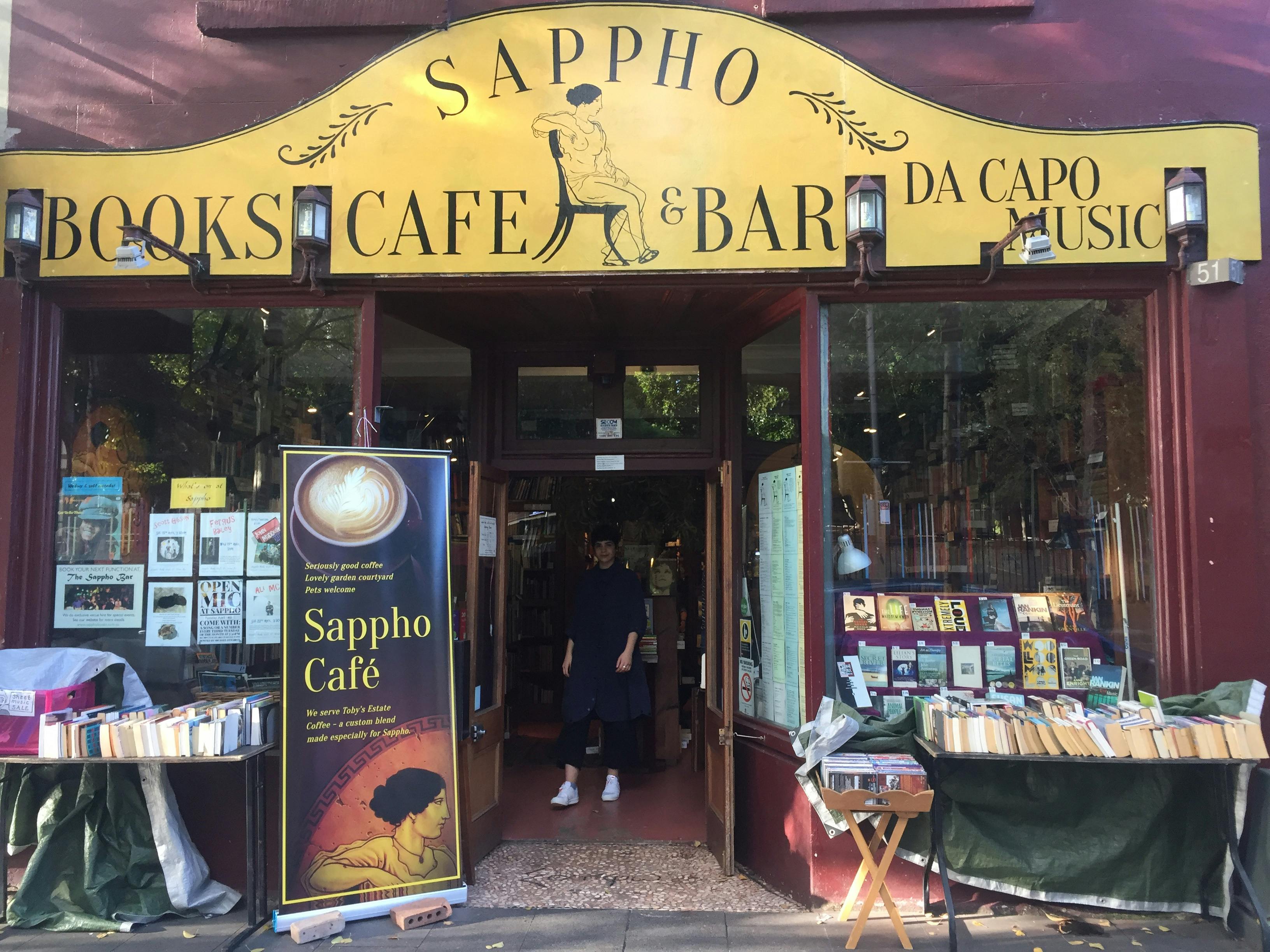 The storefront, painted maroon with a yellow sign and tables of books sitting in front of the window