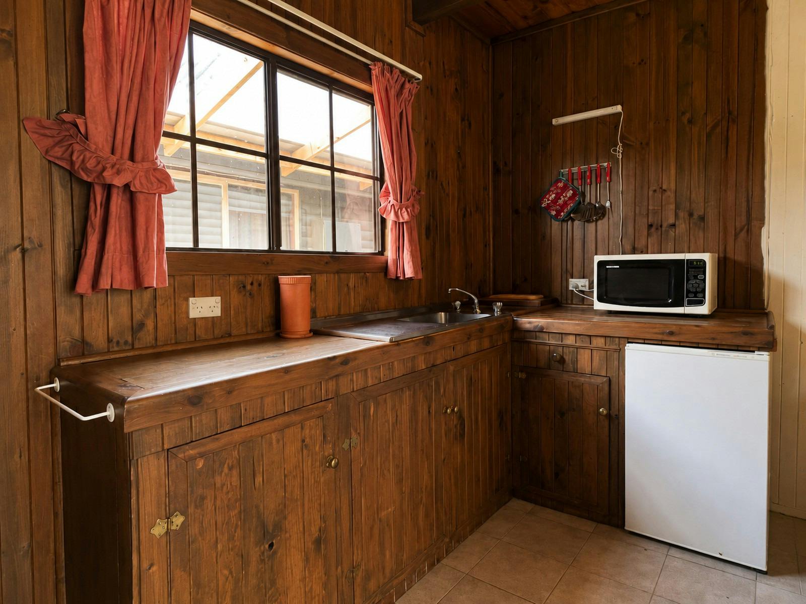 Compact timber kitchenette inside the room, showing a sink, bench, microwave, bar fridge