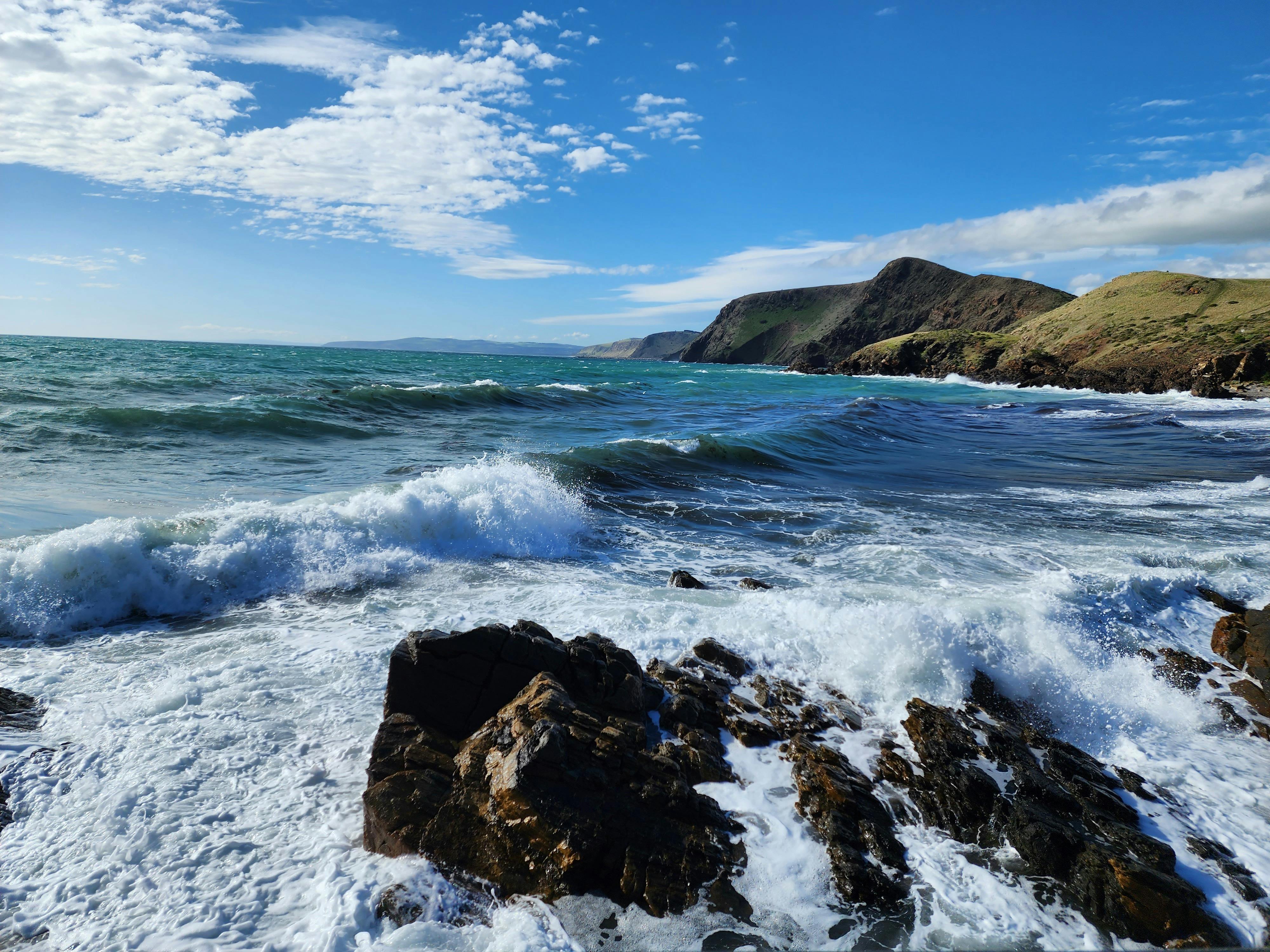 Waves crashing and foaming over rocks with cliffs in the background.