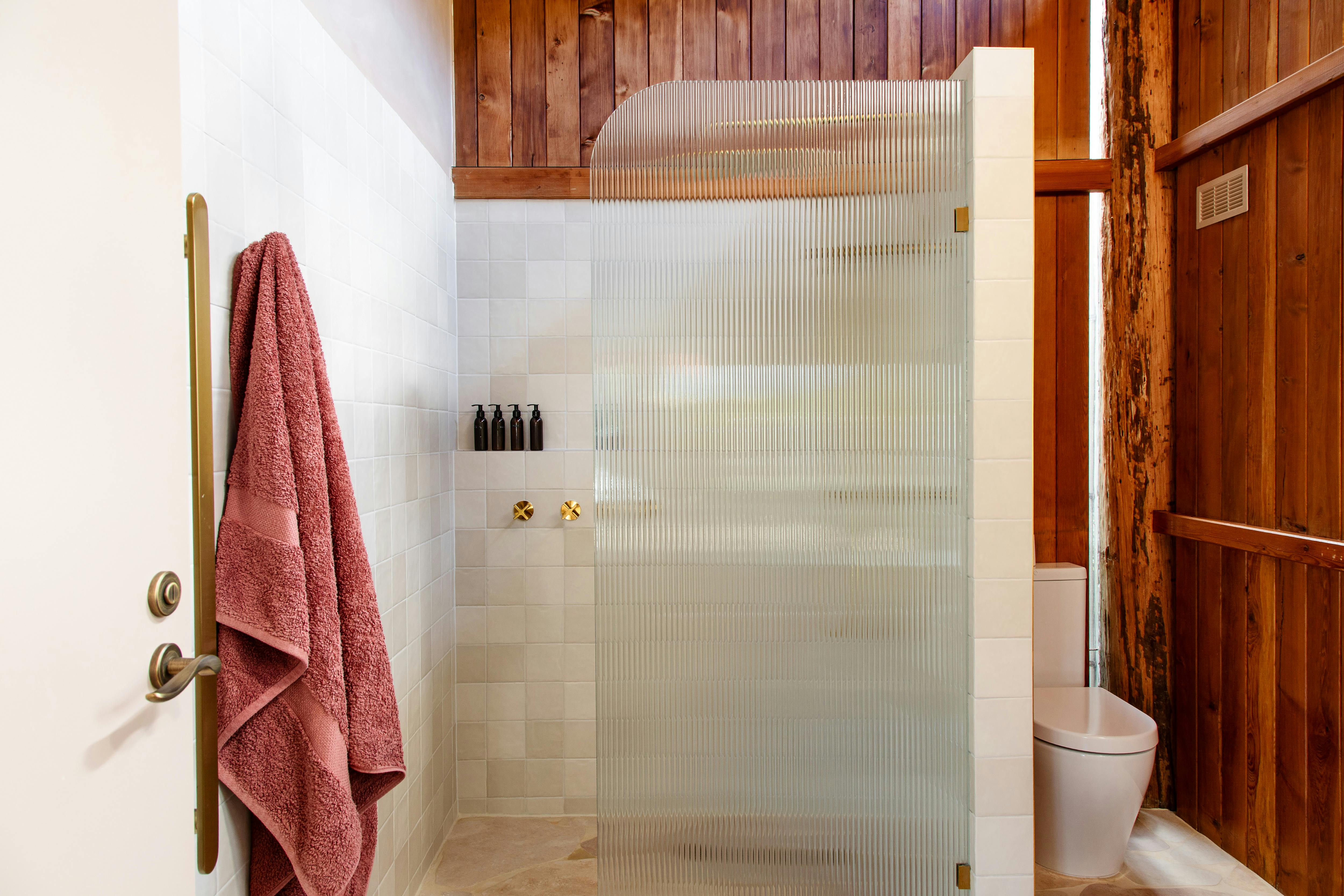 A large shower with a fluted glass and a towel hanging on the rack. A toilet is in the corner