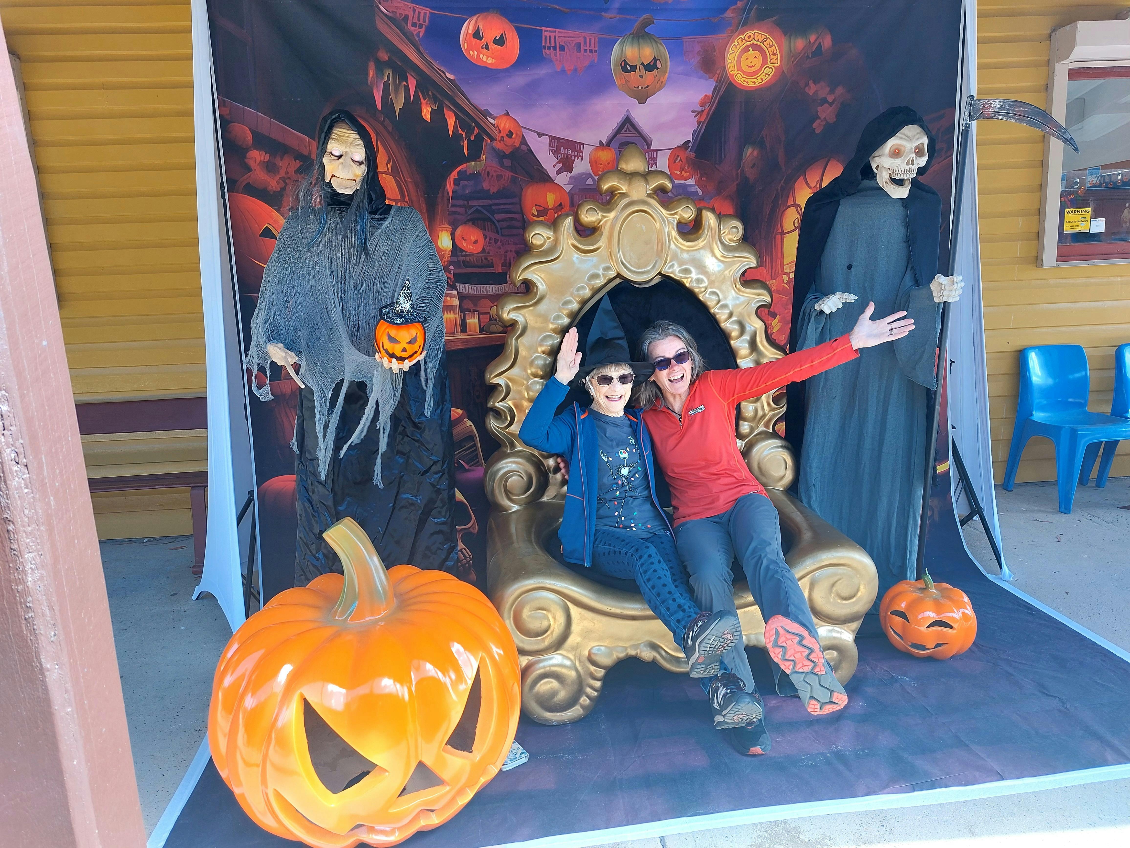 two women sitting in oversized chair with halloween figures beside