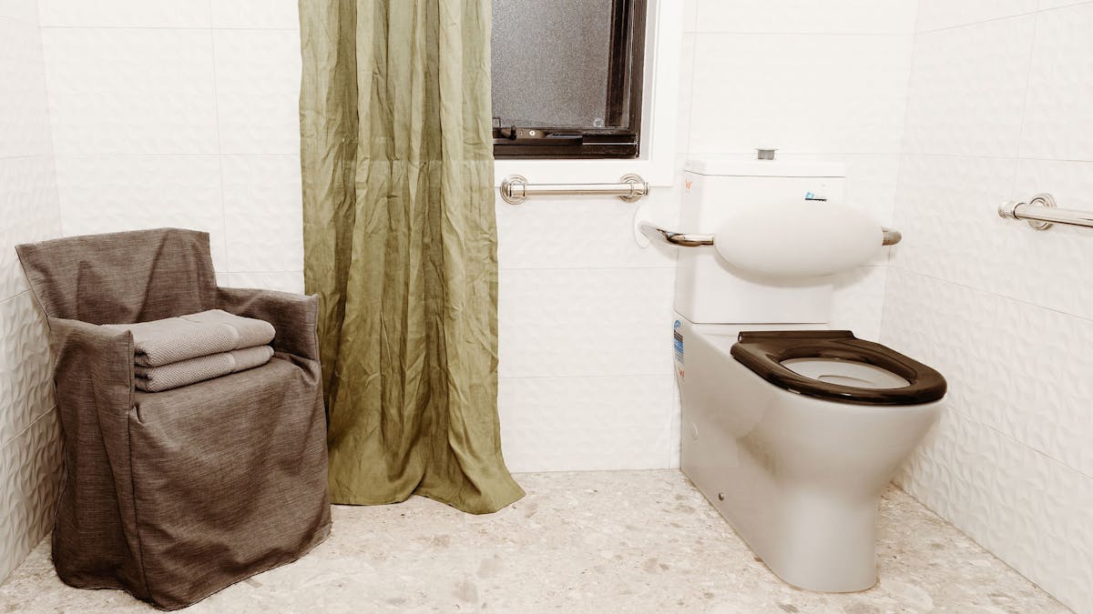 Accessible bathroom showing toilet, grab rails and alternative shower chair under a grey slip cover