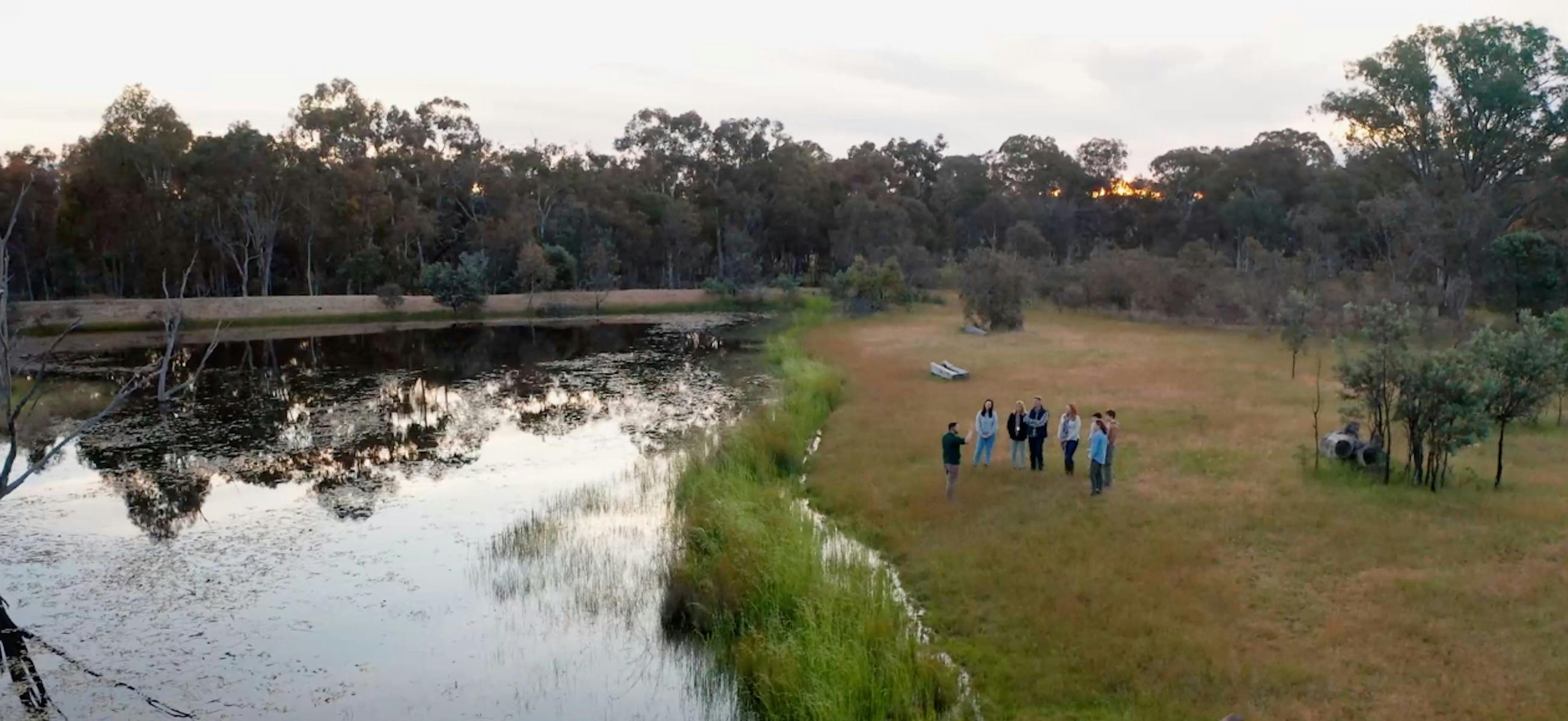 Aerial view of guide and small group standing in grasslands next to a dam