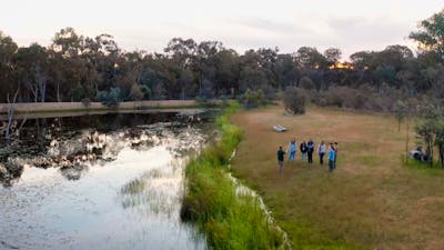 Aerial view of guide and small group standing in grasslands next to a dam