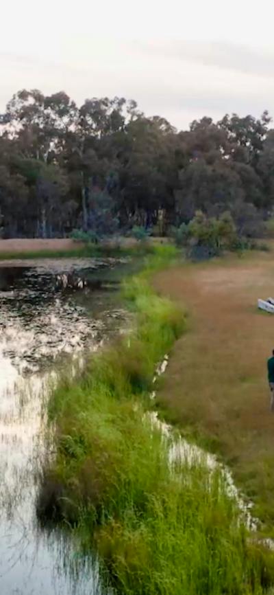 Aerial view of guide and small group standing in grasslands next to a dam