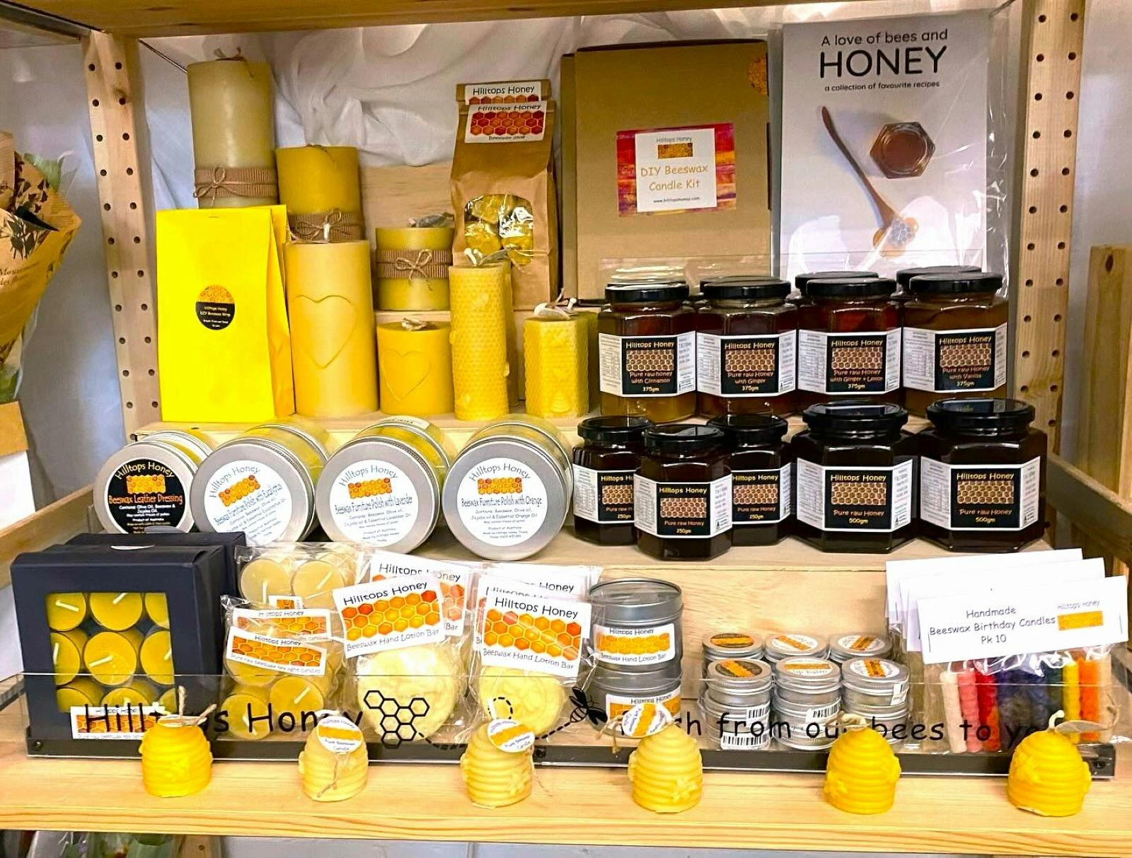 Shelf full of Hilltops Honey brand products: candles, jarred honey, furniture polish and more.