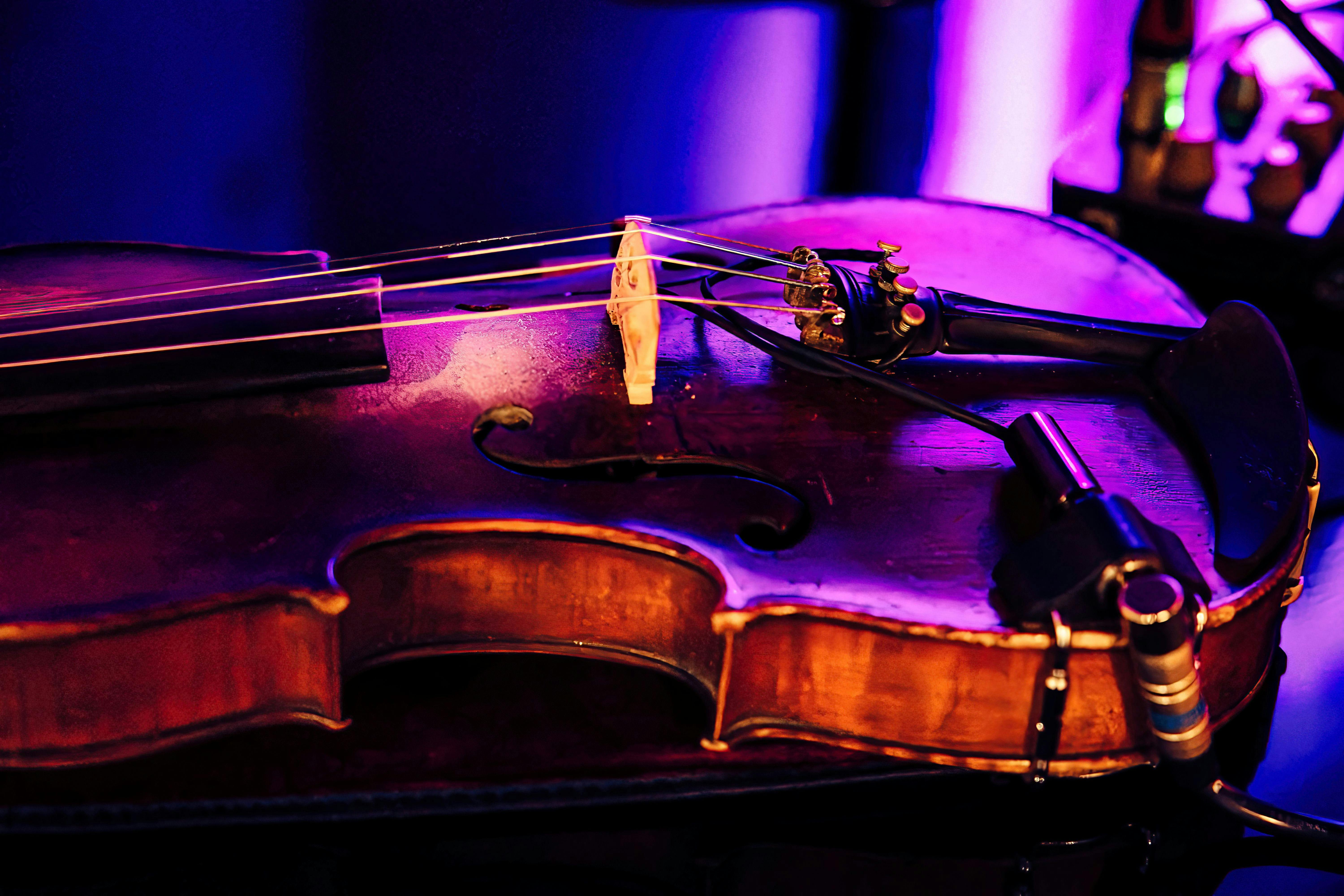 A violin lies on top of a piano, lit by purple and blue lights