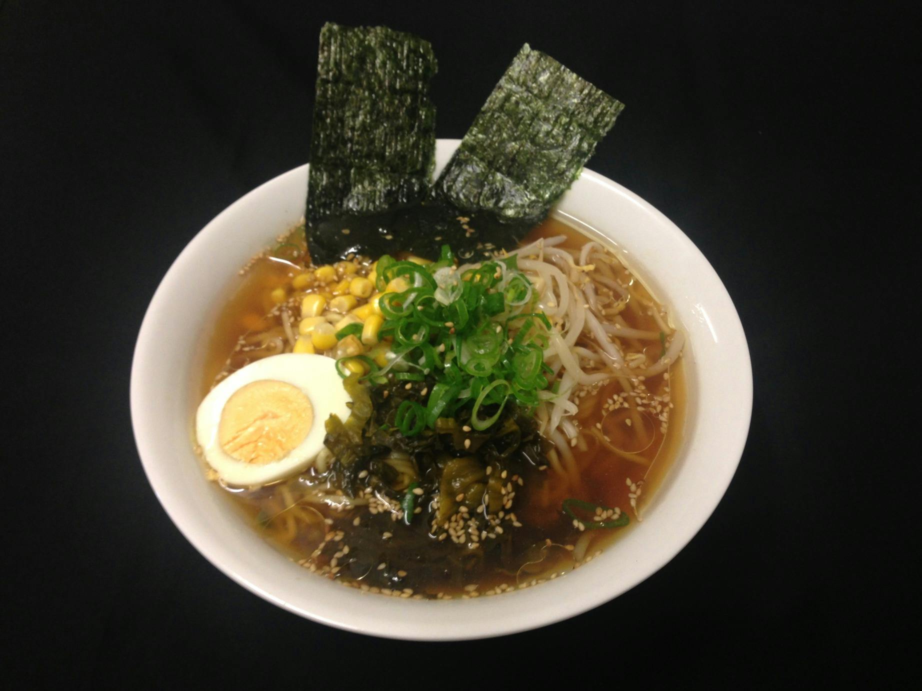 Ramen topped with half a boiled egg, sliced green onions, corn, takana, bamboo shoots and nori