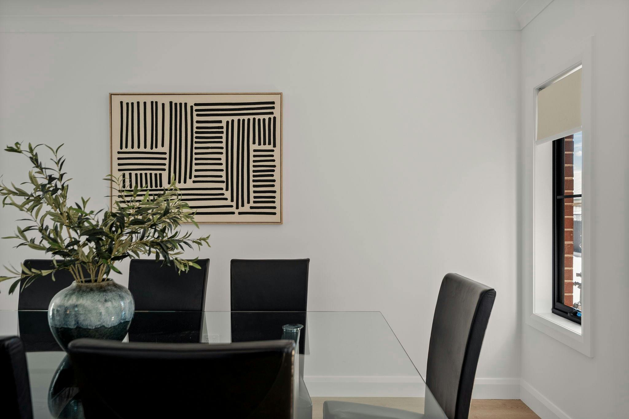 Dinign room with glass table, black dining chairs, vase with grennery and art on wall
