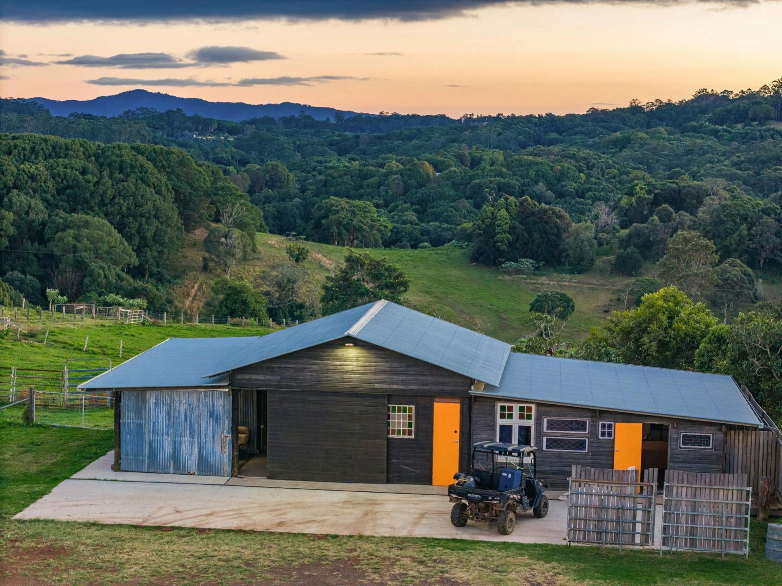 A large black shed with bright orange doors overlooks a valley at sunset