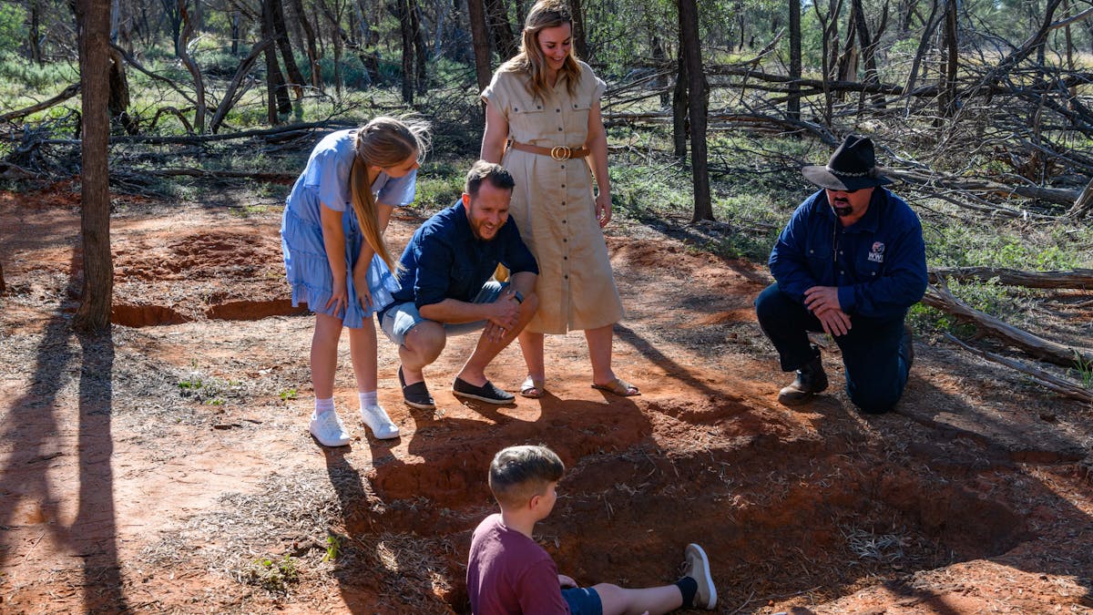 a family on tour with our guide out in the Mulga inspecting what remains of the bitumen baths