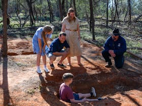 a family on tour with our guide out in the Mulga inspecting what remains of the bitumen baths