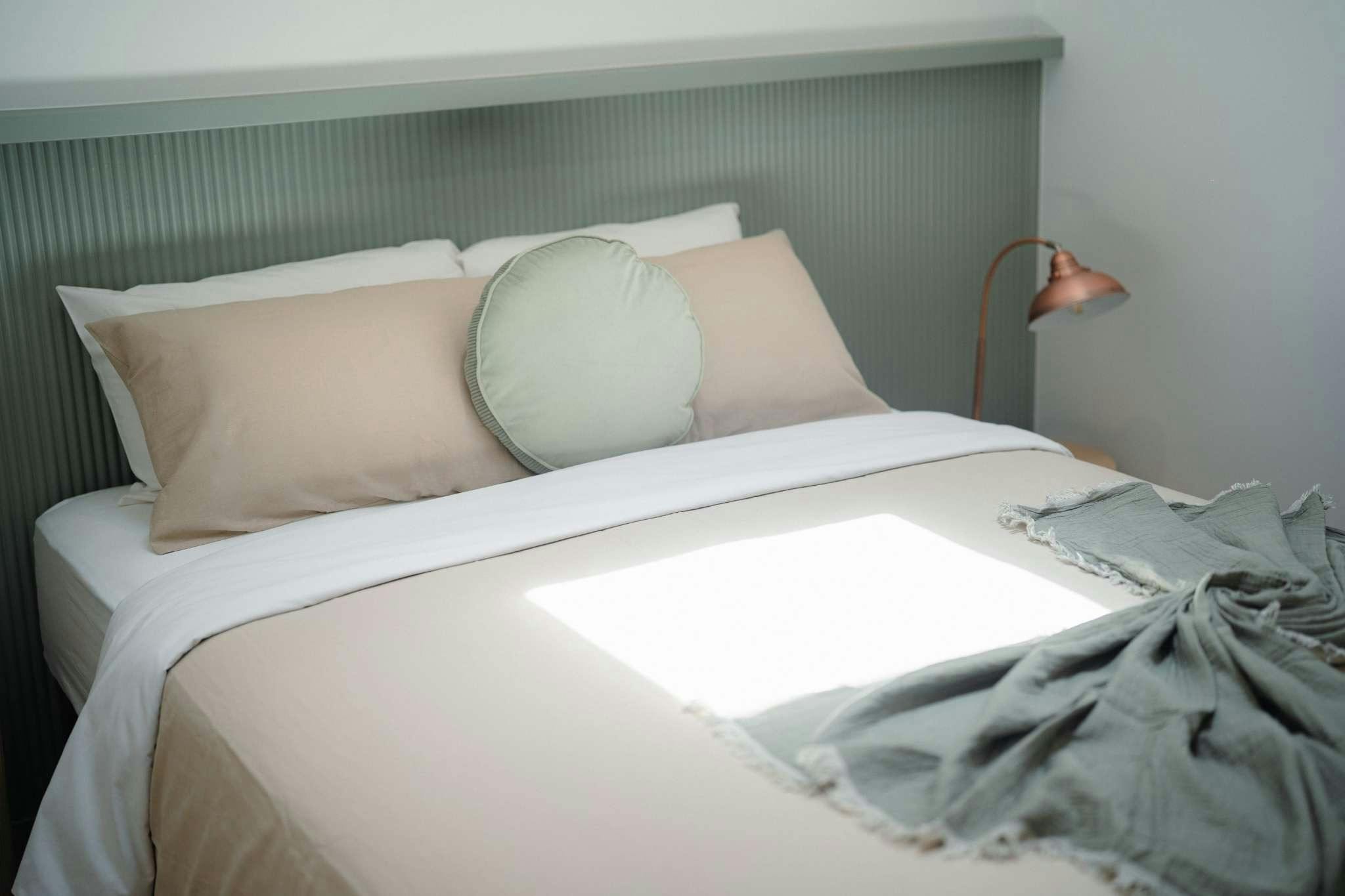 Neutral bedding with round green pillow and blue bed head