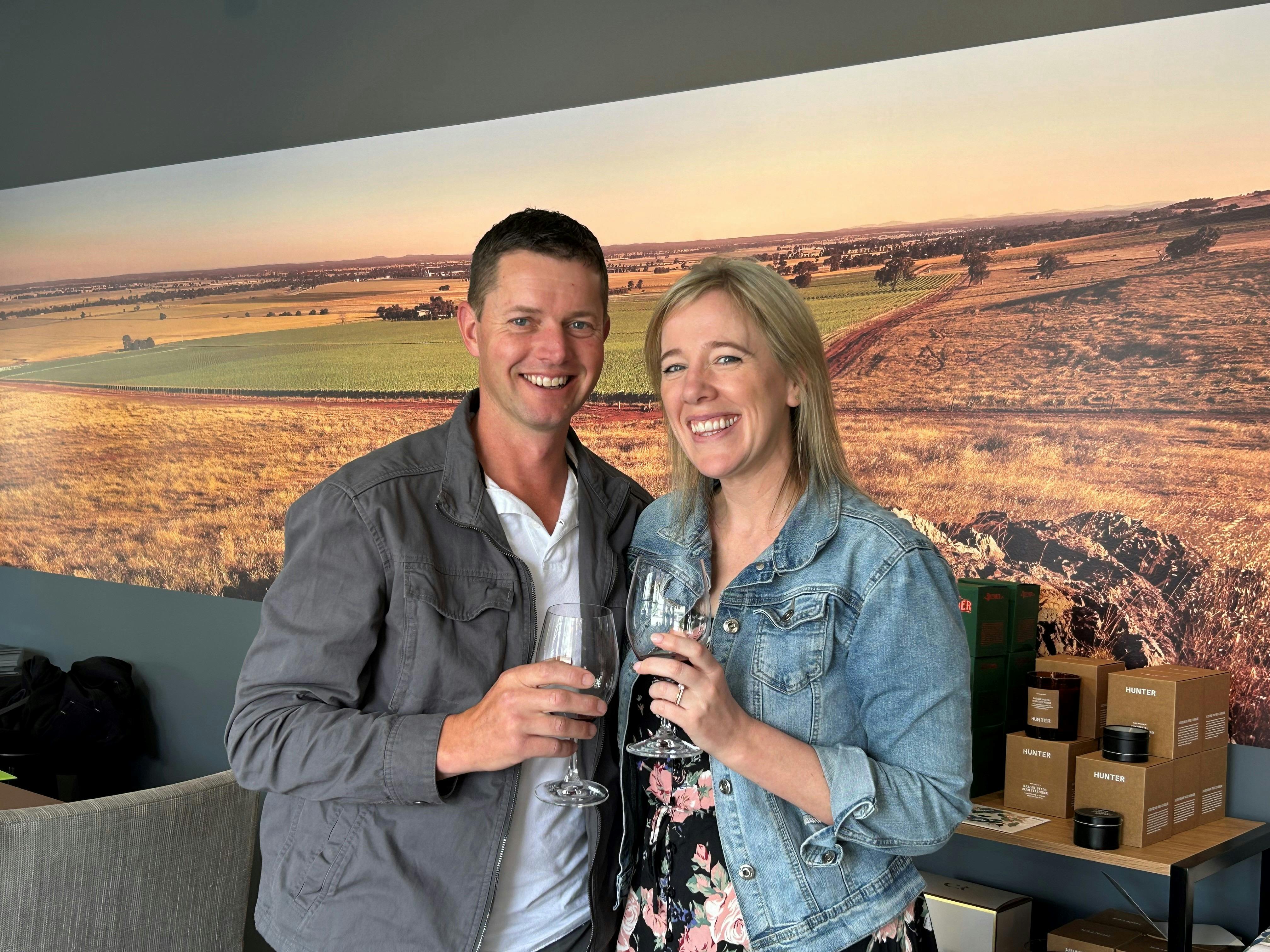 Two people smile at the camera with wine glasses in hand.