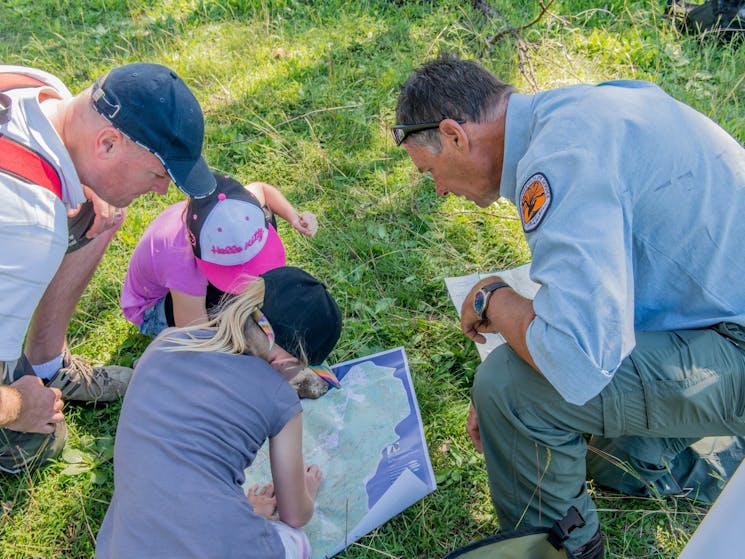 Two adults with children kneeling on grass looking a map