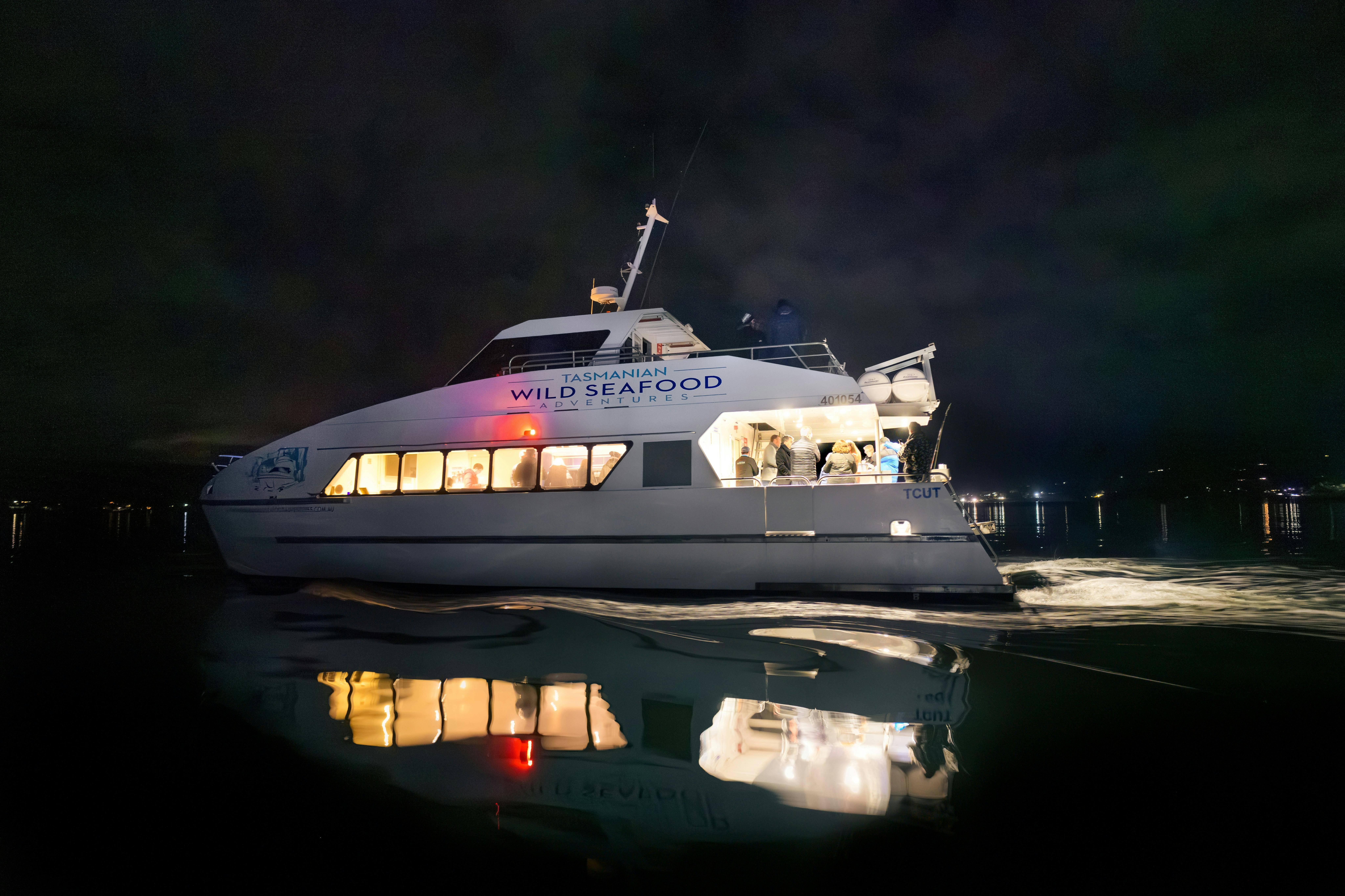 Catamaran is cruising at night with the water reflecting the vessel