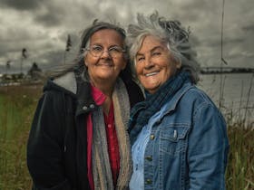 Two First Nations female Elders in front of water and a moody sky.