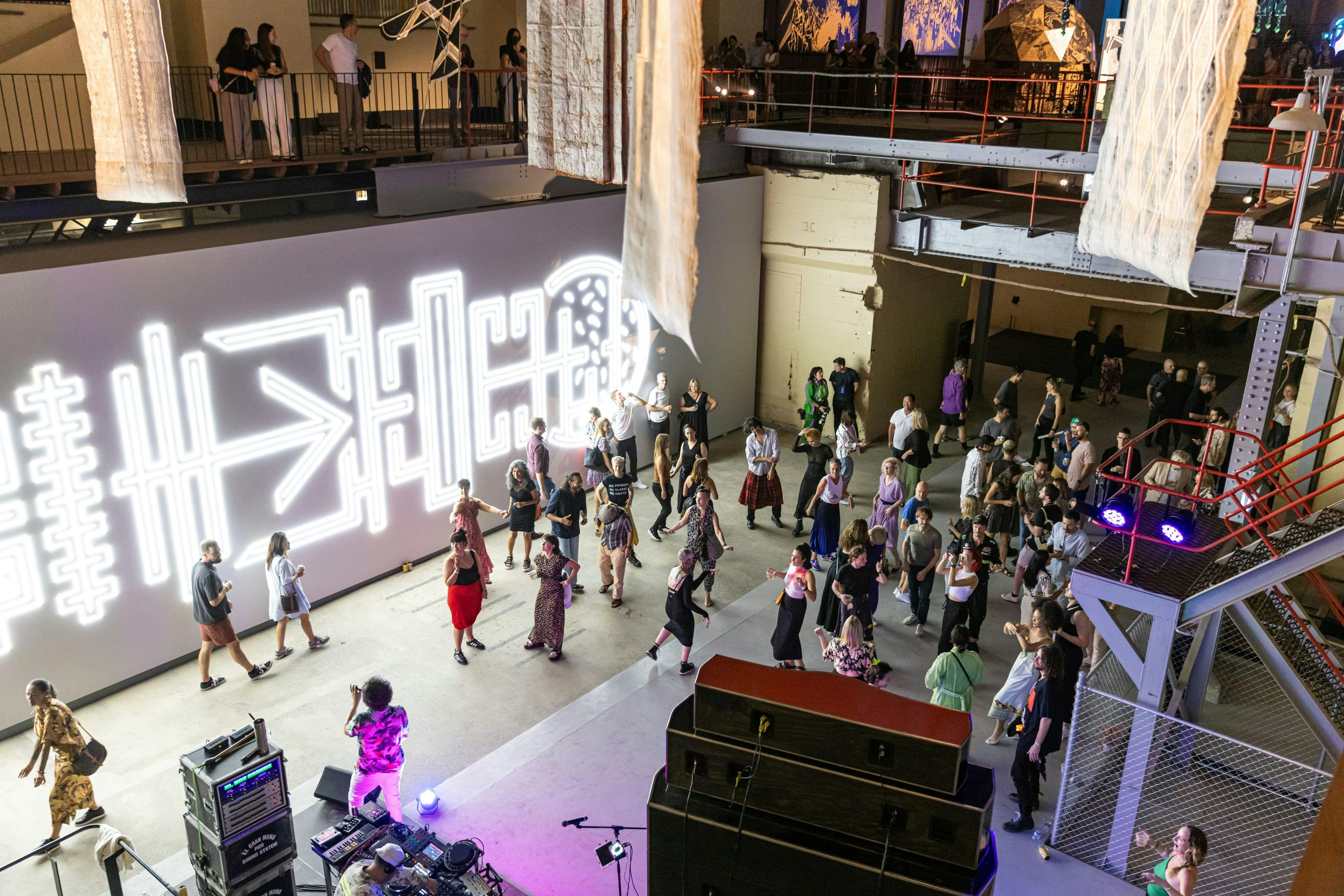 nighttime in the turbine hall of a heritage power station, illuminated by artworks, dancing people