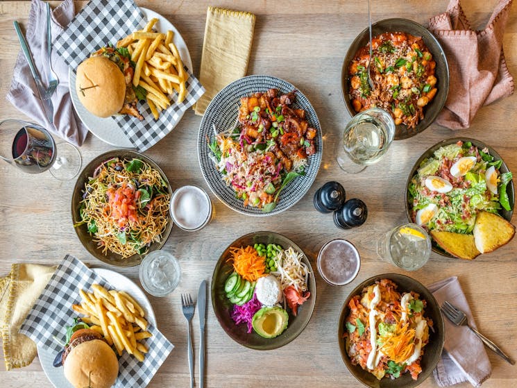 A spread of salads, burger, pasta on a wooden table at The Ophirs