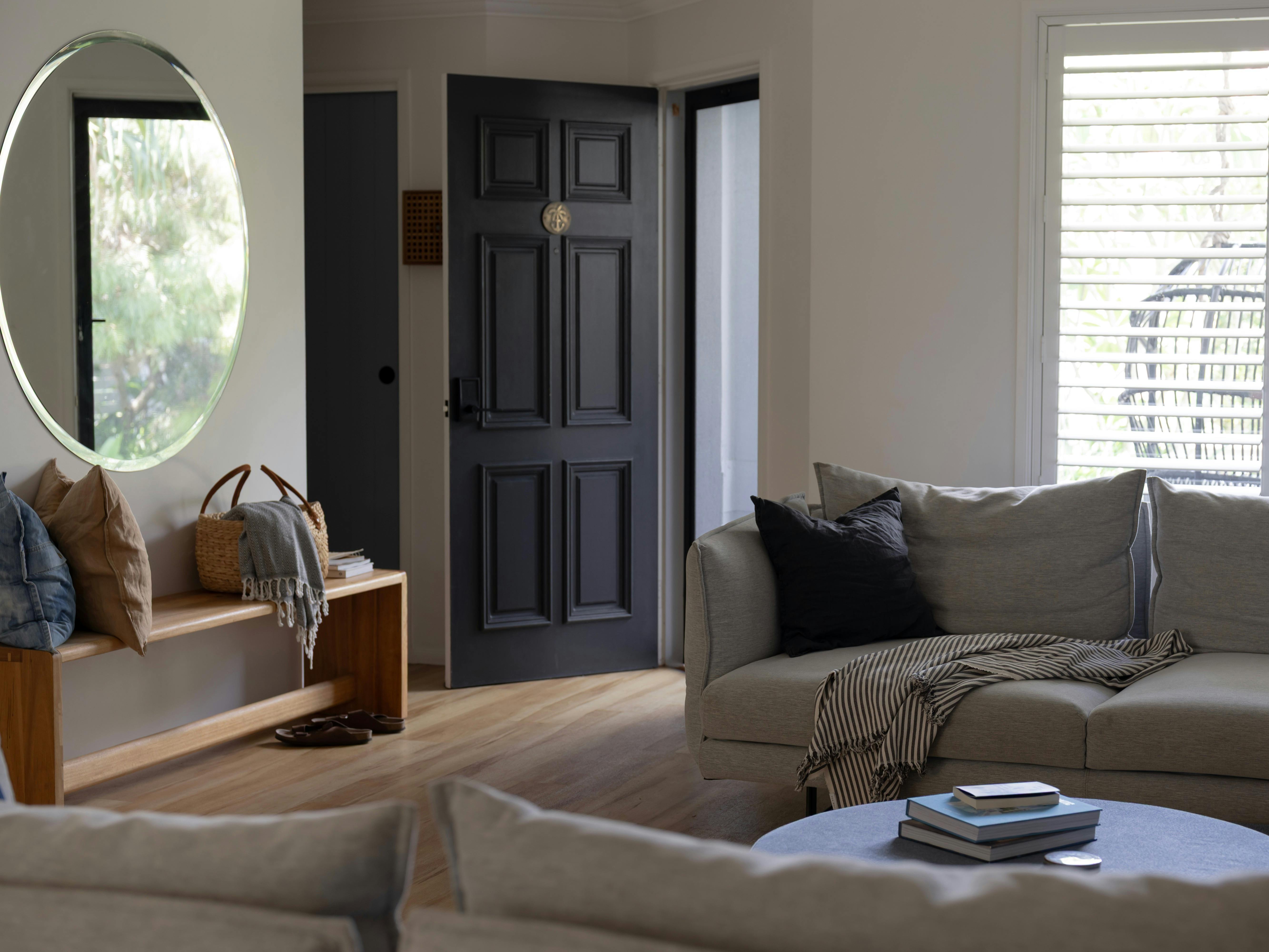 Bright and light living room with large round mirror timber bench seat and soft grey sofas