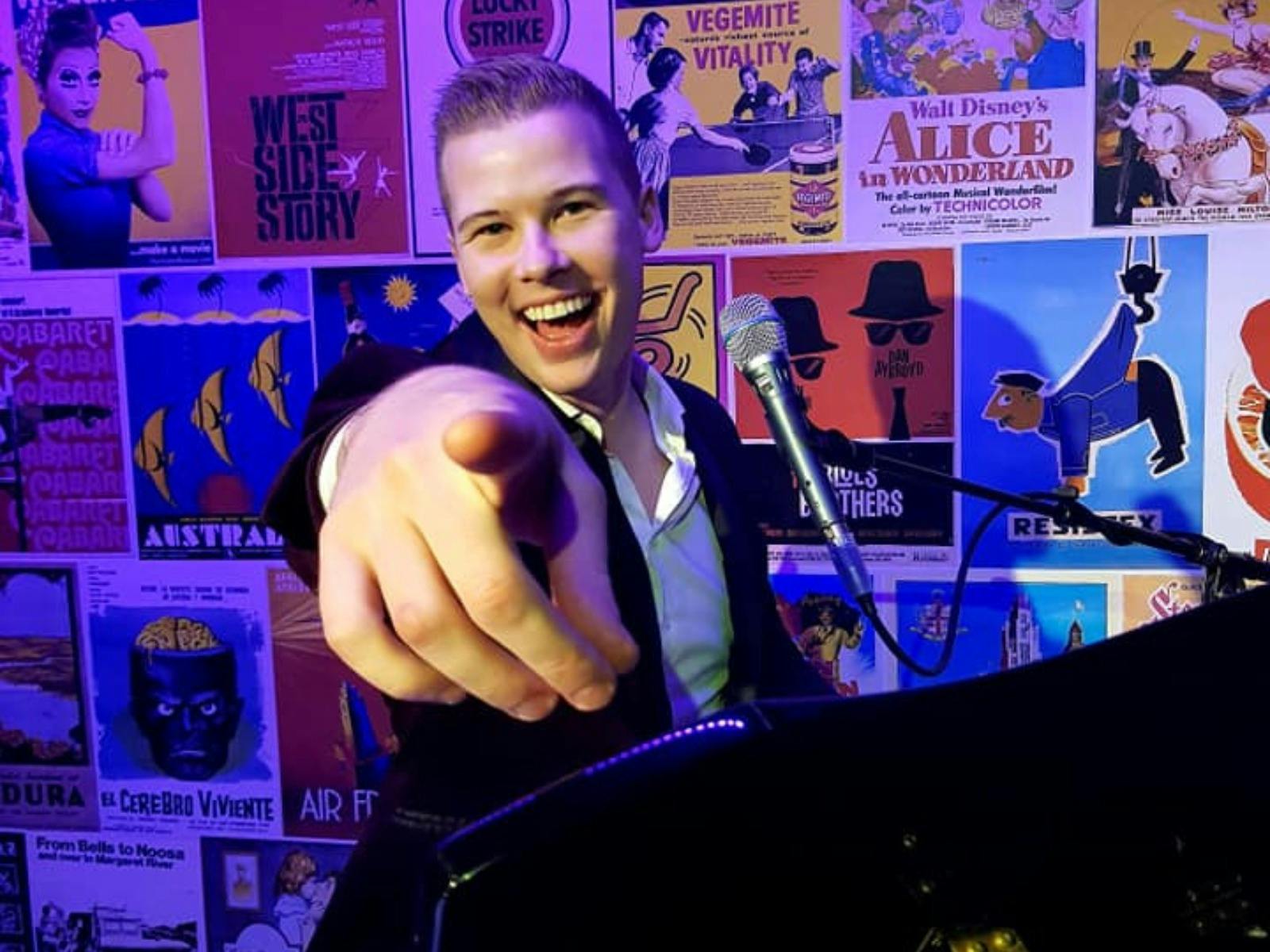Smiling man sitting at a piano and pointing a finger