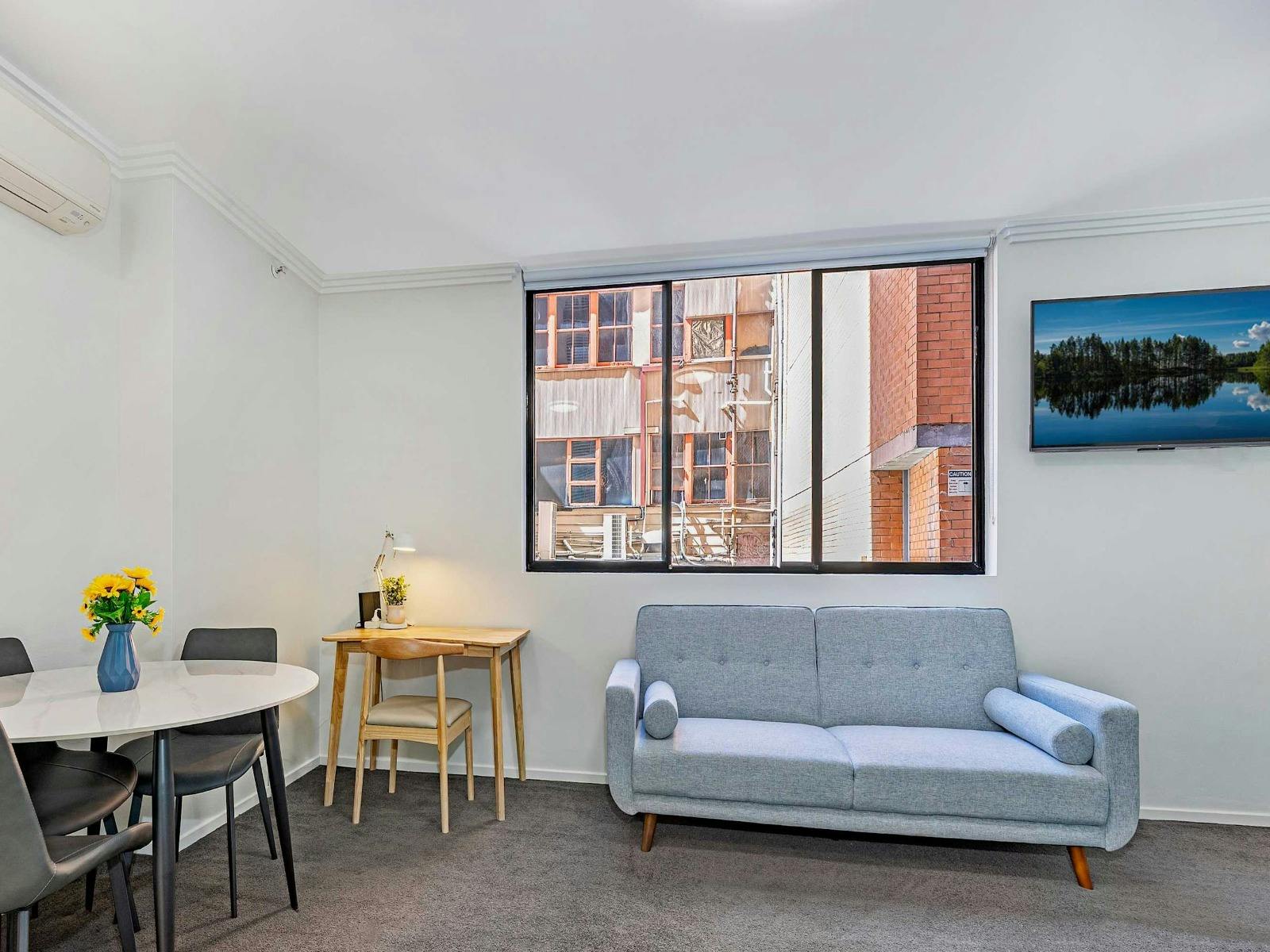 Open-plan living area with a sofa bed, dining table, and window allowing natural light.