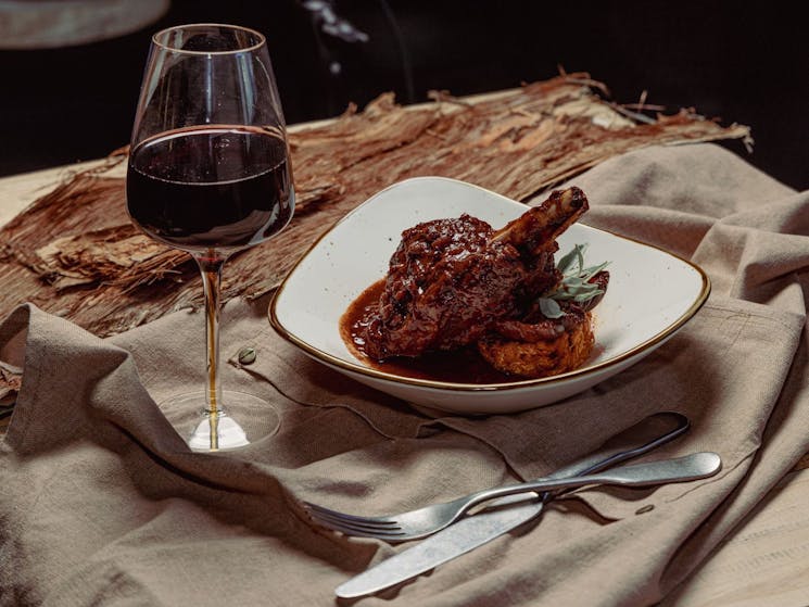 Wallaby shank on a white plate with a glass of red wine next to it