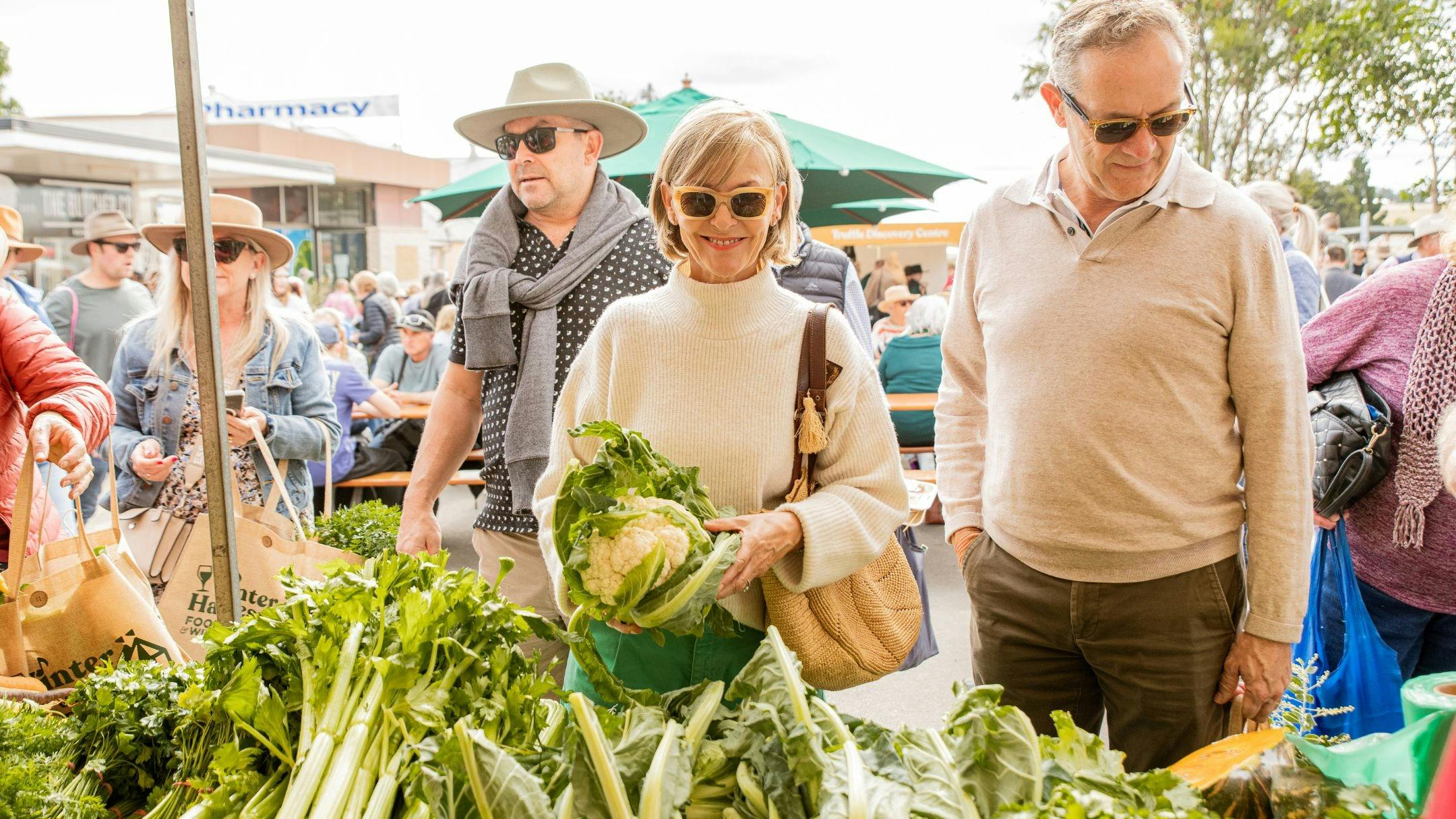 Lady at a vegetable stall smiling whilst other visitors look at range of vegetables available.