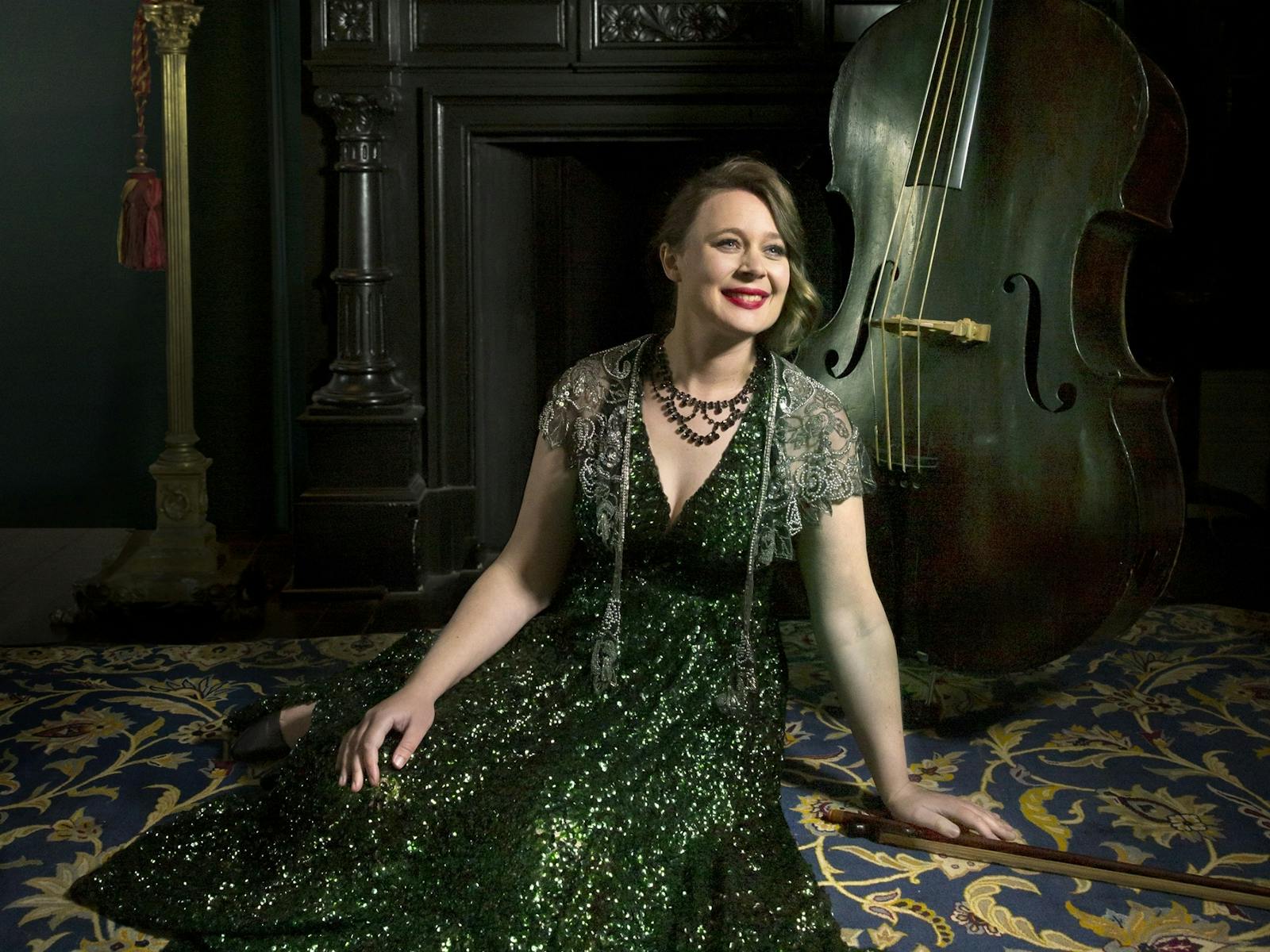 A double bass player seated n the floor in an elegant green dress.