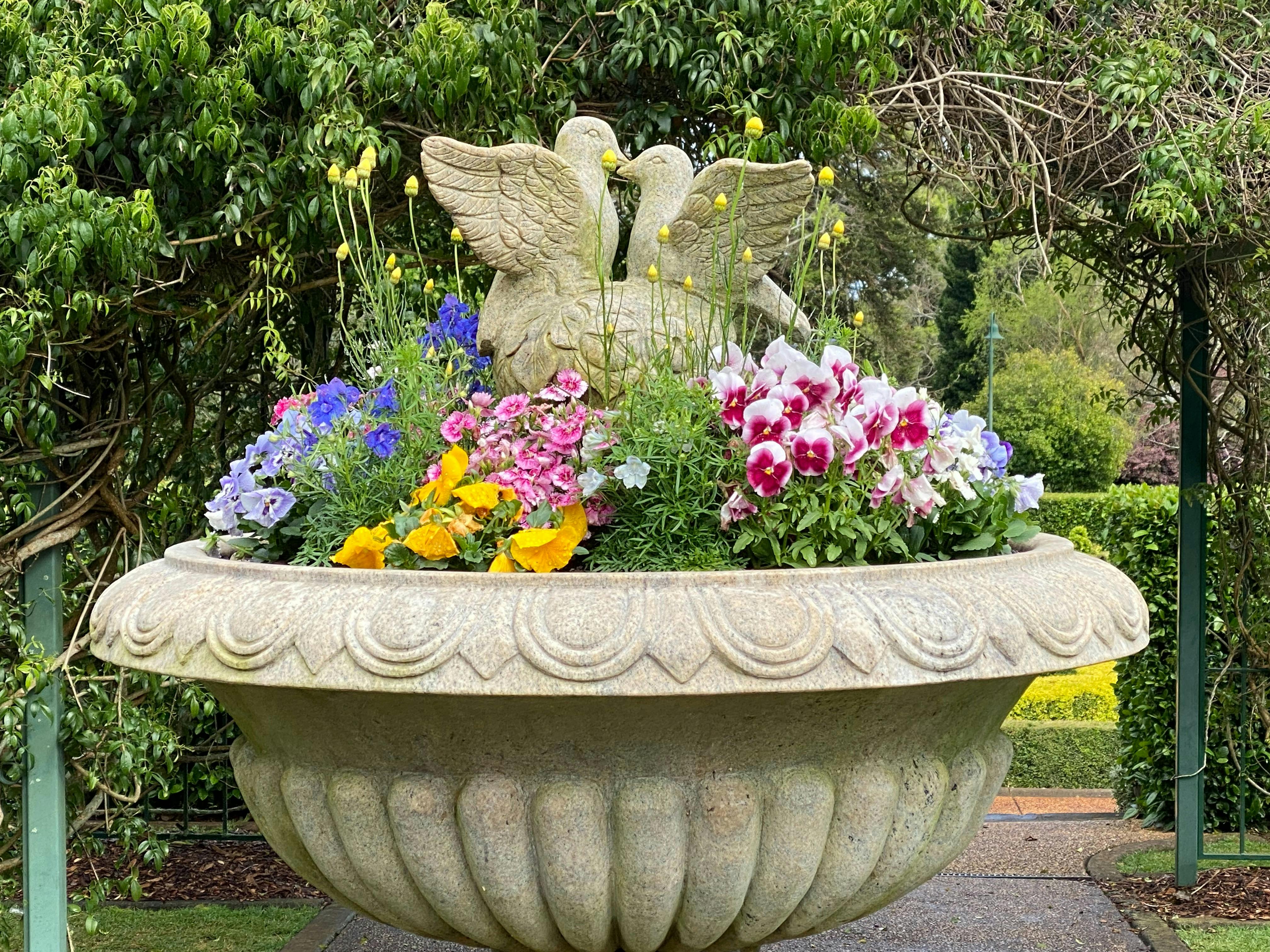 A statue of two doves surrounded by blue, yellow and pink flowers
