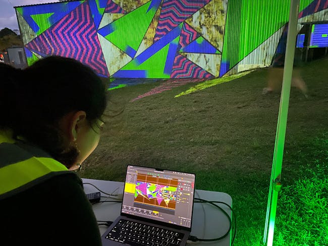 A person looking at a laptop screen which is projecting bright colours to a wall in the background