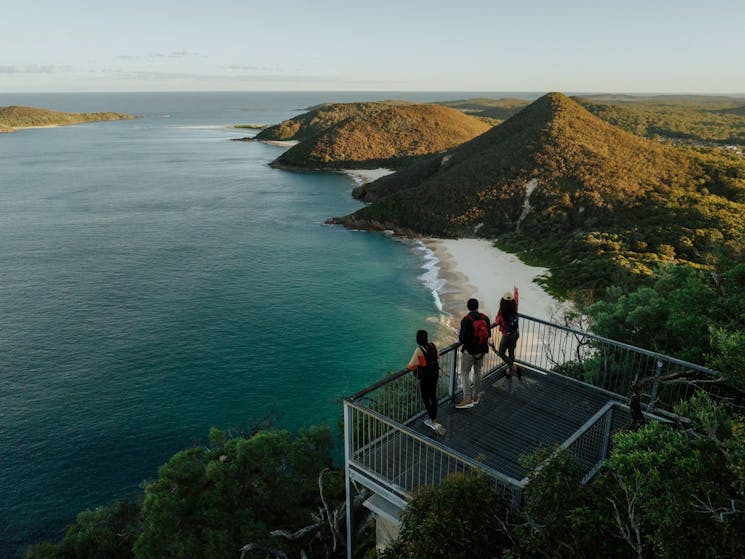 Three people at the viewpoint of Tomaree Head Summit, looking at the coastline