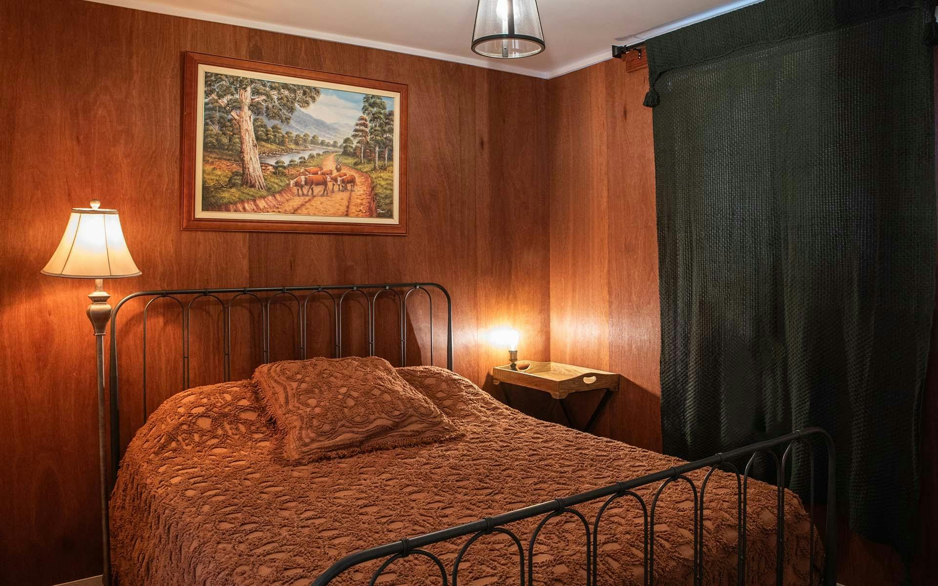 A double bed with a lamp beside it and a painting above it