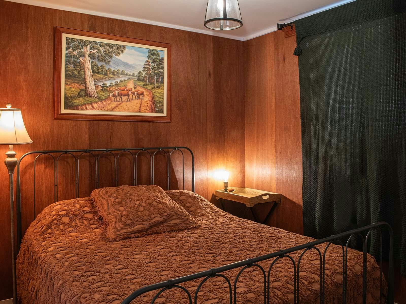 A double bed with a lamp beside it and a painting above it A double bed with a lamp beside it and a painting above it