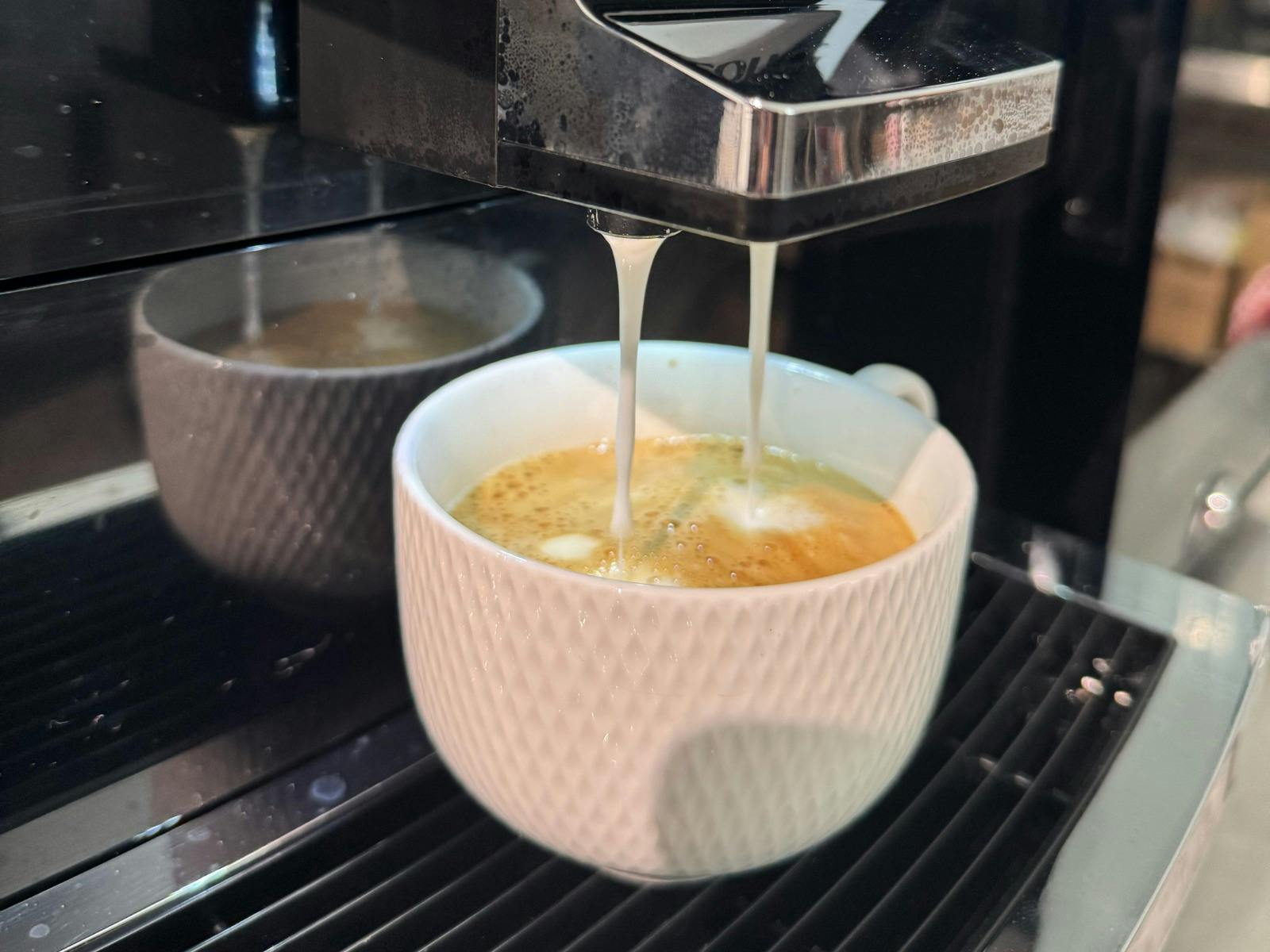 Freshly brewed coffee filtering from the coffee machine into the cup with frothy milk