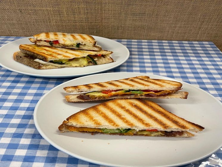 2 fresh vegetable toasties sitting on a white plate on a blue and white checked table cloth