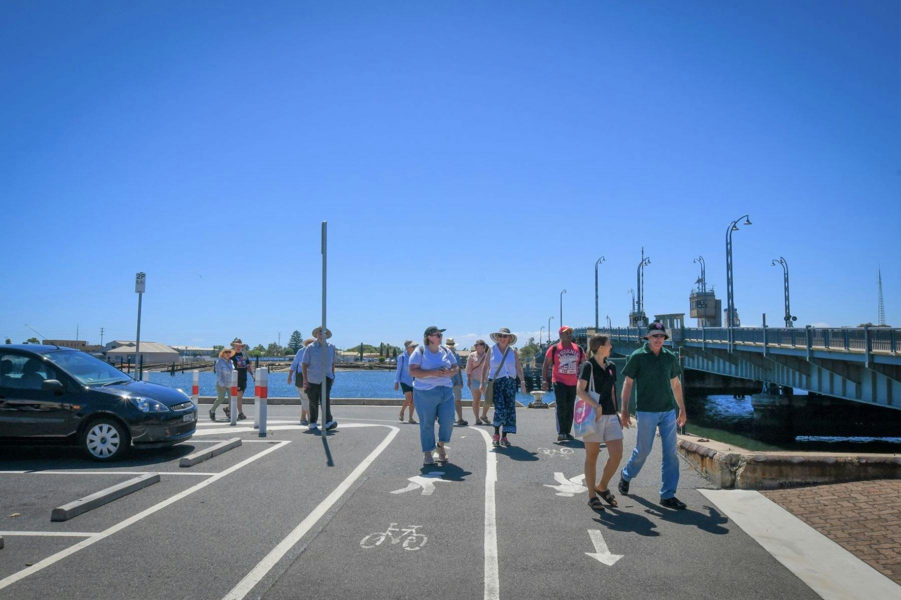 A tour guide leads a group around the Port River on foot.