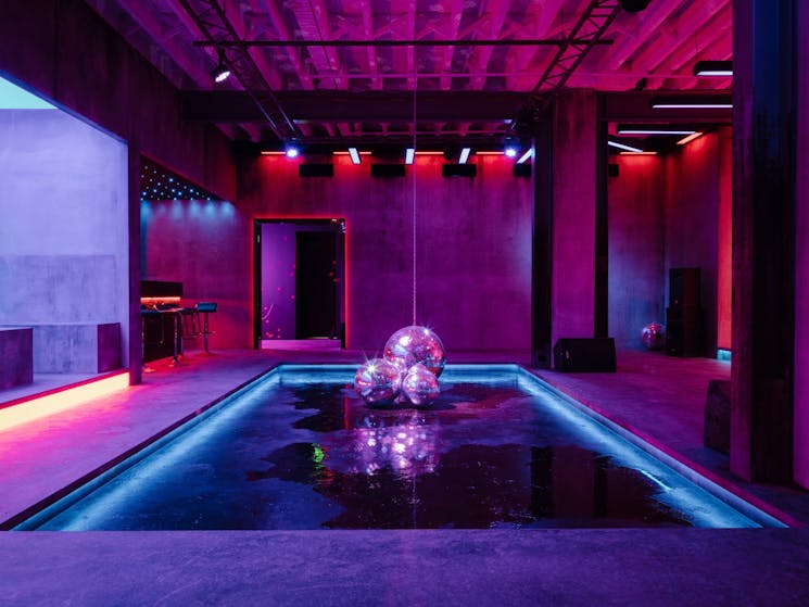 An artwork installation of a dancehall with neon club lighting and disco balls on the floor