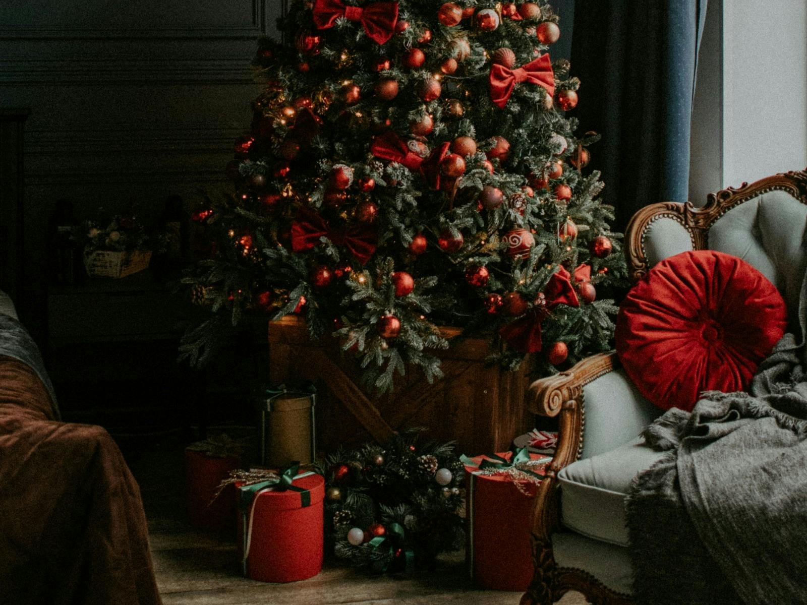 A dark yet welcoming Christmas setting featuring a christmas tree with presents and a comfy chair.