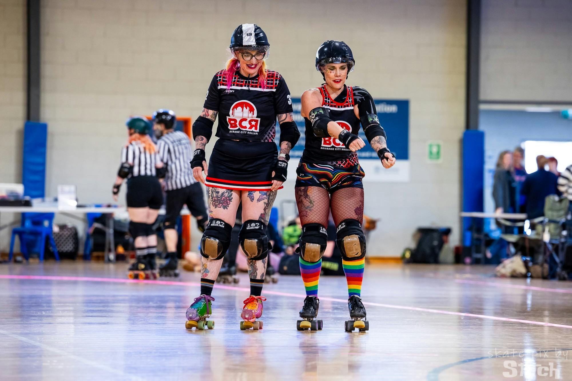 two roller derby players wearing black and red and rainbow accessories