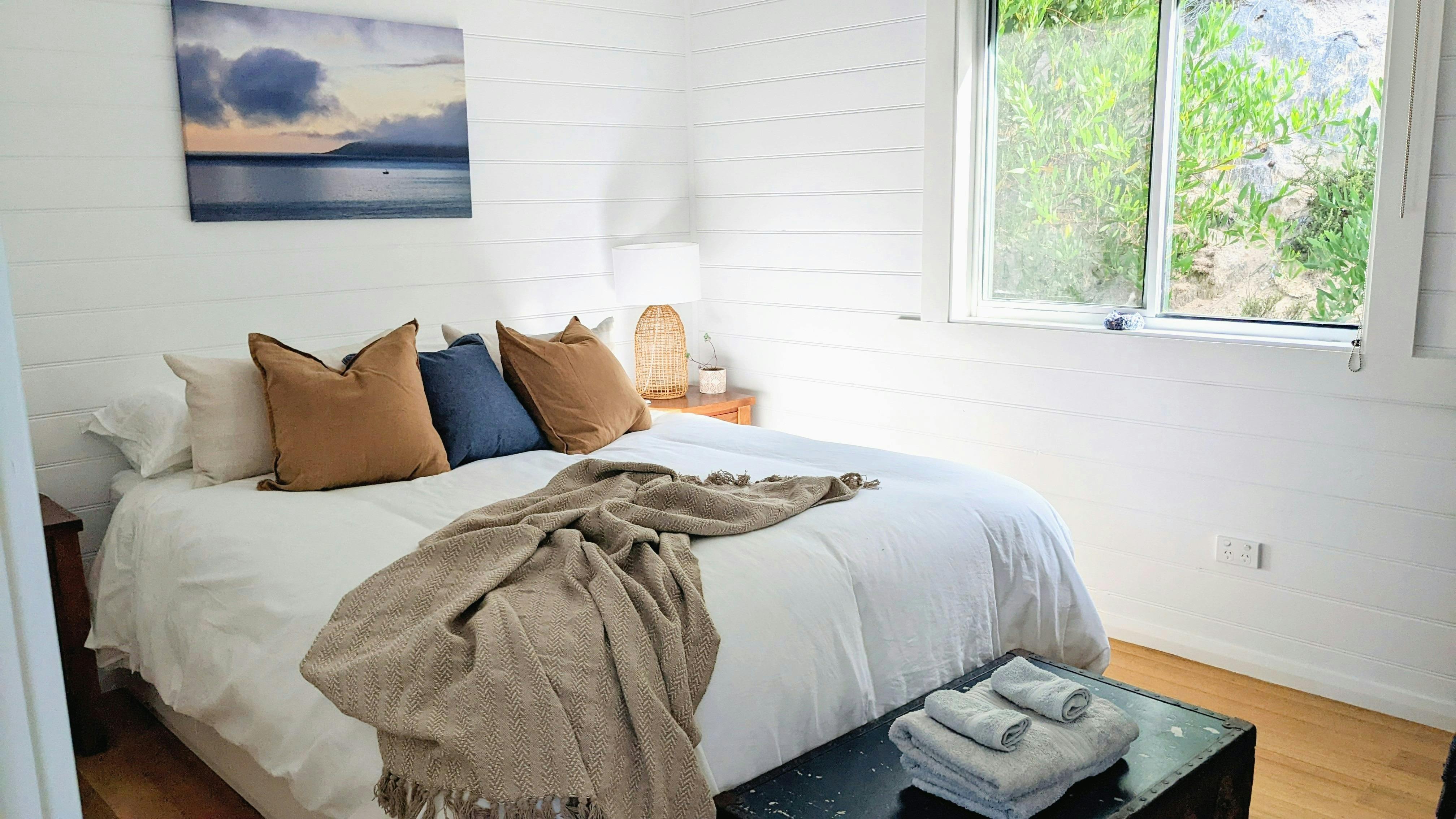 White painted bedrrom with queen size bed. Bed has brown and blue cushions and brown throw