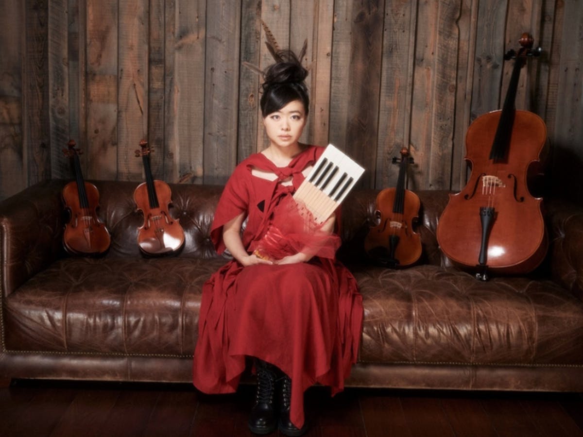 One female sitting on a couch, holding a violin. There are two violins by each side.