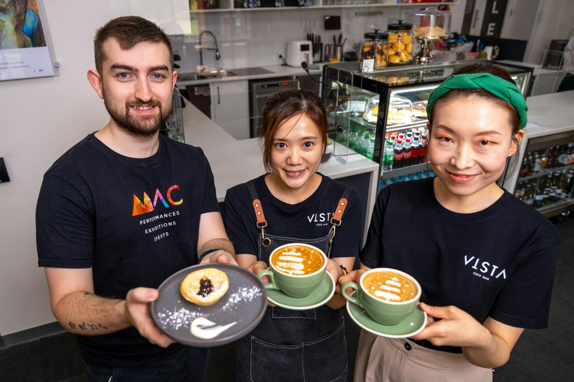 One male, and two female staff members showcasing cups of coffee and food