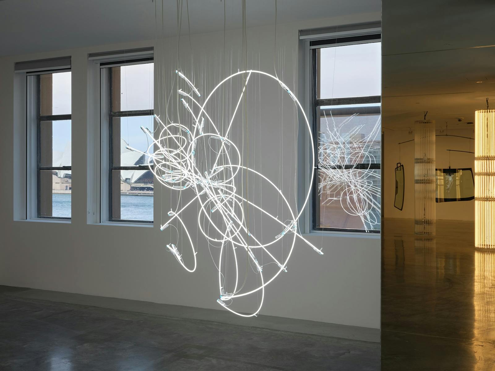 Neon lights hanging in a gallery with a view out to Sydney Harbour