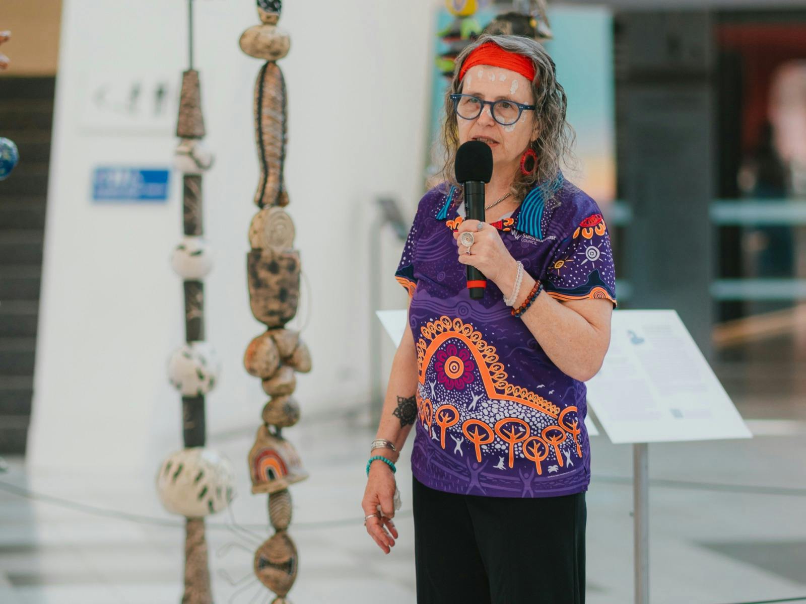 Woman dressed in aboriginal polo shirt standing in front of stone sculptures