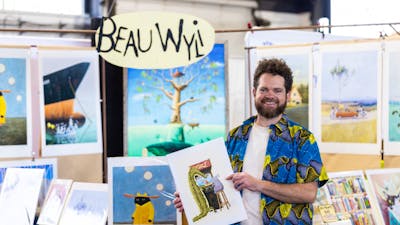 Beau Wylie standing in front of his stall at the Handmade Market Canberra holding his art